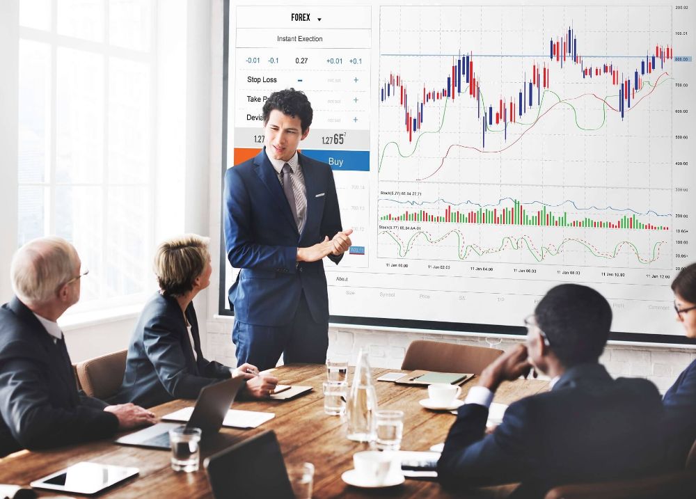 Presenter explaining market charts to colleagues in a meeting room